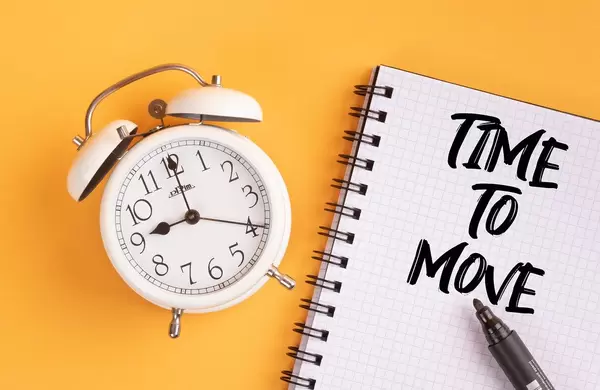 Wecker und ein Notizblock mit dem Text "Time to move / Zeit zum Umziehen", mit einem Filzstift vor gelbem Hintergrund