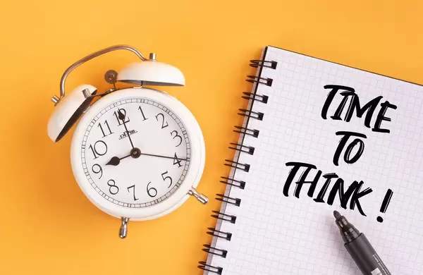 Wecker und ein Notizblock mit dem Text "time to think / Zeit zu denken", mit einem Filzstift vor gelbem Hintergrund