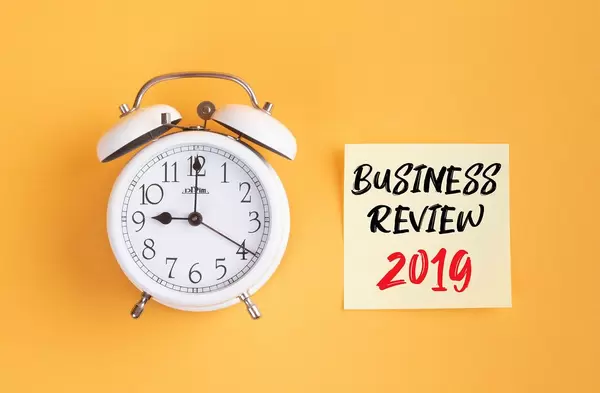 Wecker und ein Zettel mit ‘Business Review 2019’ Text vor gelbem Hintergrund