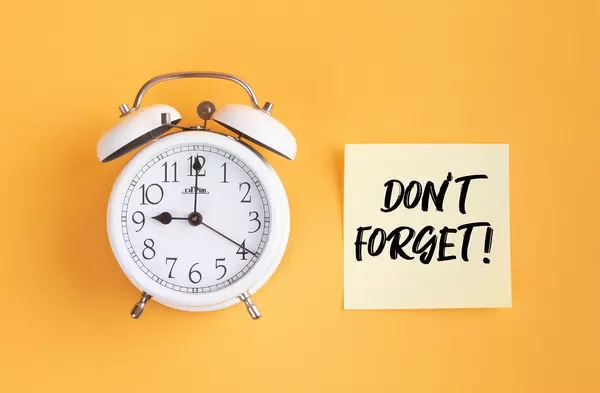Wecker und ein Zettel mit ‘Don’t forget!’ Text vor gelbem Hintergrund