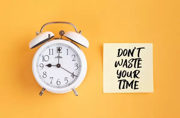 Wecker und ein Zettel mit ‘Don’t waste your time!’ Text vor gelbem Hintergrund