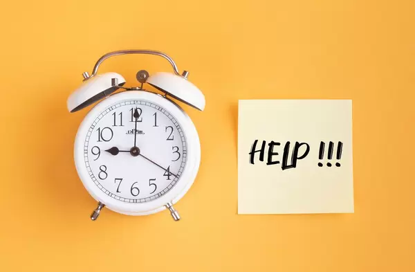 Wecker und ein Zettel mit ‘Help!!!’ Text vor gelbem Hintergrund