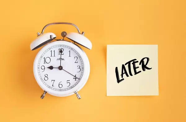Wecker und ein Zettel mit ‘Later’ Text vor gelbem Hintergrund