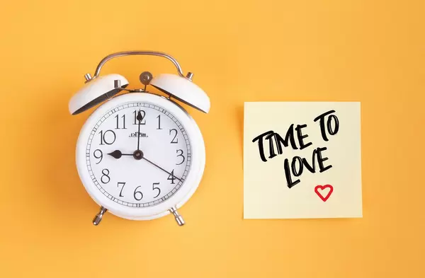 Wecker und ein Zettel mit ‘Time to love’ Text vor gelbem Hintergrund