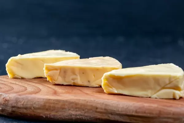 Weichkäse in Dreiecksform auf Holzbrett vor dunklem Hintergrund