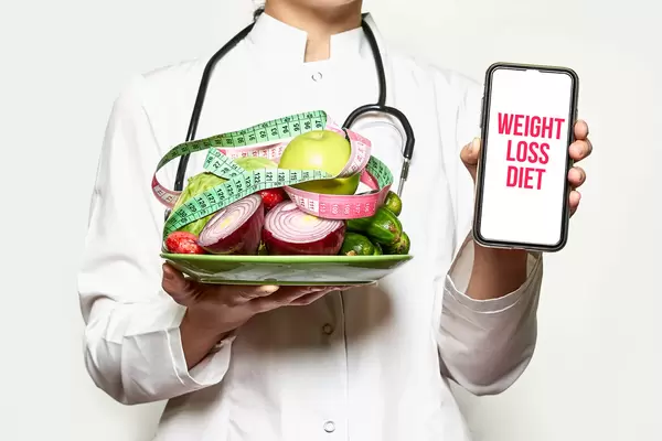Weight loss diet - Doctor holds fresh fruits and vegetables and smartphone
