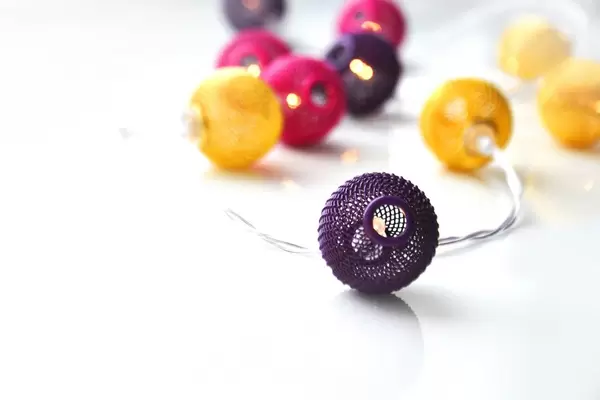 Weihnachtliche Lichterkette aus bunten Mini-Laternen in violett, gelb und pink vor weißem Hintergrund