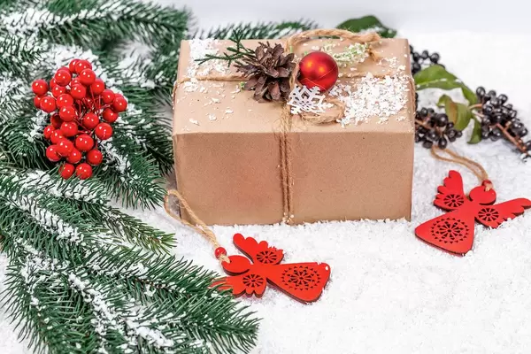 Weihnachtsgeschenk mit Tannenzapfen und Christbaumkugel geschmückt im Schnee mit roten Engeln und Tannenzweigen