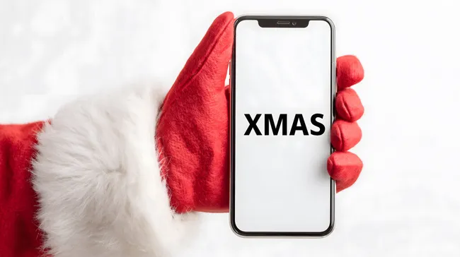 Weihnachtsmann-Hand hält Smartphone mit Xmas-Schrift