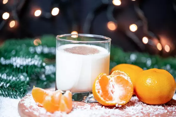 Weihnachtsmotiv - Ein Glas Milch mit Mandarinen und Tannenzweigen im Hintergrund