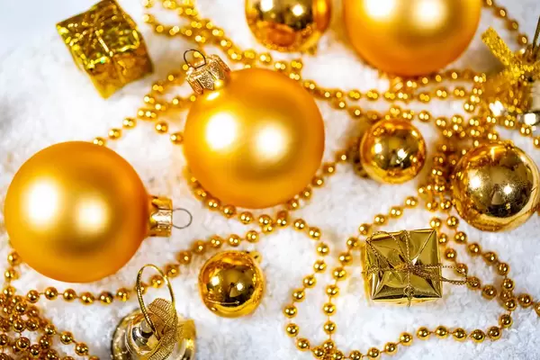 Weihnachtsmotiv - goldene Christbaumkugeln mit Geschenken und Kette im Schnee