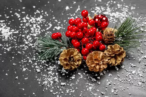 Weihnachtsstimmung: Weihnachtsdekoration aus Tannenzweigen und Zapfen mit Schneeflocken auf schwarzem Tisch
