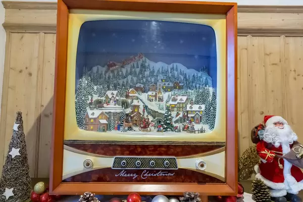 Weihnachtsszene mit verschneitem Dorf auf nostalgischem Fernseher neben Tannenbaum und Nikolaus
