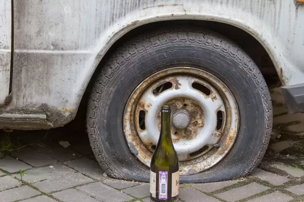 Weinflasche neben einem schrottreifen Auto mit einem Platten