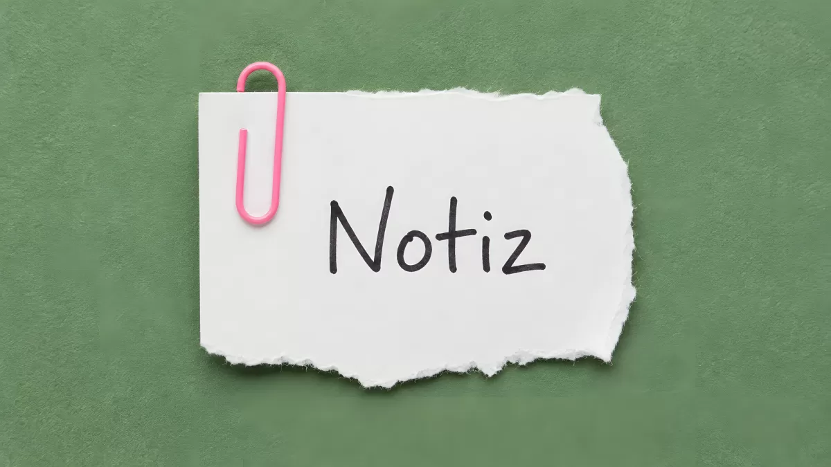 Weißer Notizzettel mit rosa Büroklammer auf grünem Hintergrund