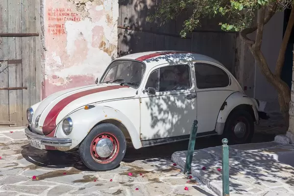 Weiß-roter Volkswagen Käfer Oldtimer in einer Gasse vom Dörfchen Chalki auf Naxos, Griechenland