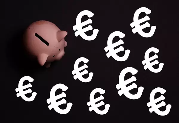 Weiße Eurosymbole auf schwarzem Hintergrund, neben einem rosa Sparschwein aus der Sicht von oben