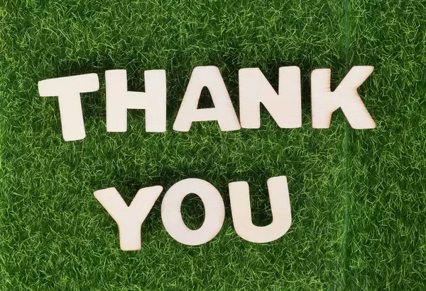 Weiße Holzbuchstaben bilden den Text THANK YOU (vielen Dank) auf grüner Wiese
