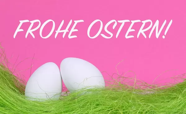 Weiße Ostereier auf grünem Gras vor Text Frohe Ostern auf rosa Hintergrund