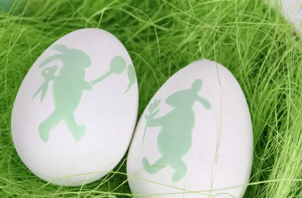 Weiße Ostereier mit Osterhasen-Muster auf grünem Gras Nahaufnahme