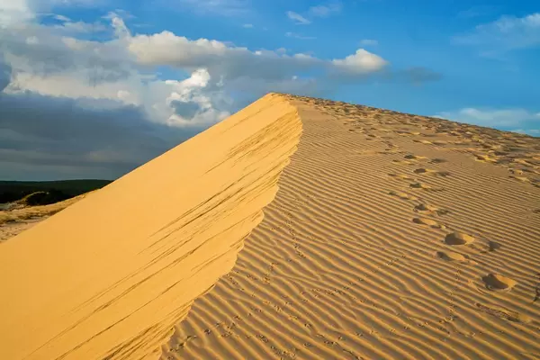 Weiße Sanddünen in Mui Ne, Vietnam mit Fußspuren und goldenen Reflektionen des Sonnenuntergangs