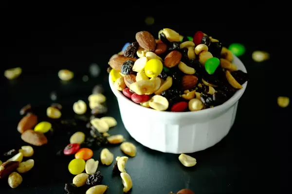 Weiße Schale, überfüllt mit Nussmix mit Rosinen und bunten Süßigkeiten vor dunklem Hintergrund