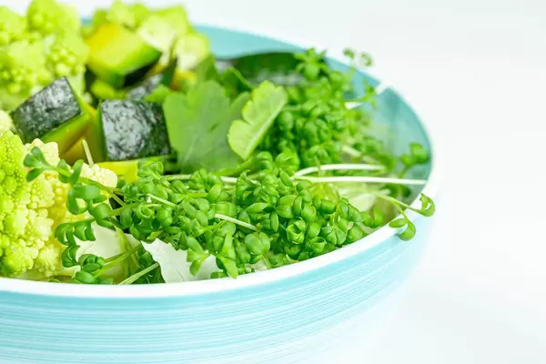 Weiße Schüssel mit frischem Salat, Romanesco Kohl, Avocado, Petersilie und Wasserkresse mit weißem Hintergrund Nahaufnahme