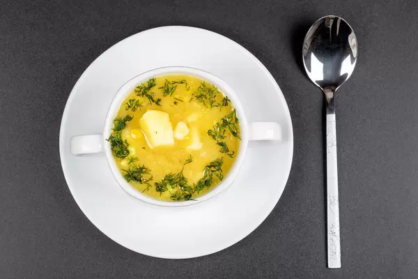 Weiße Suppentasse mit Erbsensuppe mit Kartoffeln und Dill auf einem weißen Teller mit Löffel von oben fotografiert