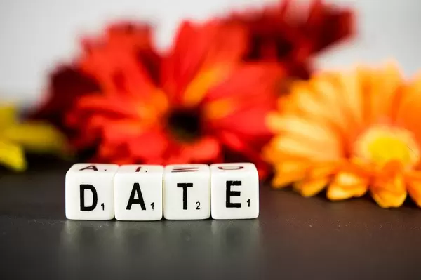 Weiße Würfel mit Buchstaben zeigen das Wort Date "Treffen", mit roten und orangen Blumen im Hintergrund