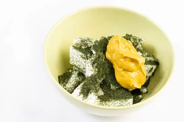 Weißer Käse mit Dill-Kräuter und Senf in einer Schale auf weißem Untergrund