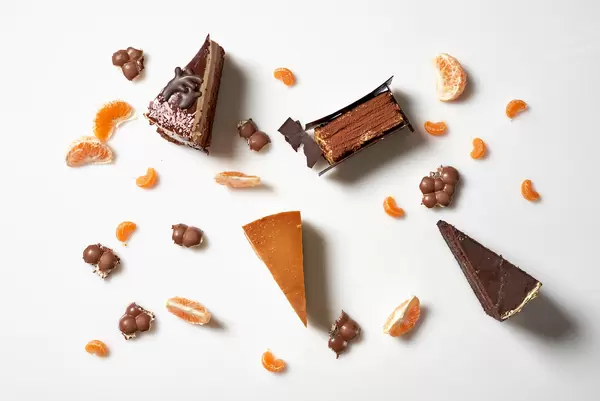 Weißer Patisserie-Hintergrund mit vier Tortenstücken und Orangen- und Mandarinenstücken