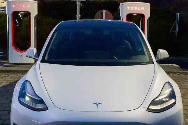 Weißer Tesla Model 3, Frontansicht und Supercharger-Ladesäulen mit LED-Beleuchtung