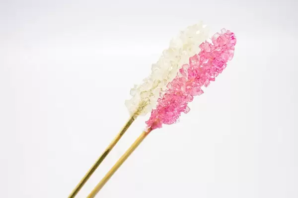 Weißer und pinker Kandiszucker auf einem Holzstab vor weißem Hintergrund