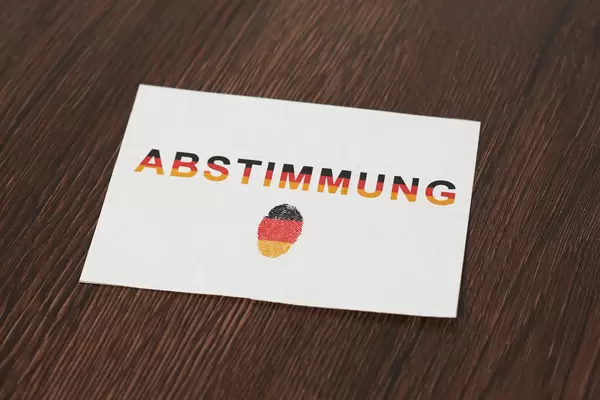 Weißer Zettel mit Schrift "Abstimmung" und Fingerabdruck in der Farben der deutschen Flagge