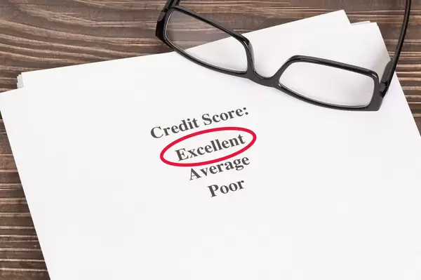 Weißes Papier mit ausgezeichnetem Kreditscore-Ergebnis rot umkreist mit Lesebrille auf einem Holztisch