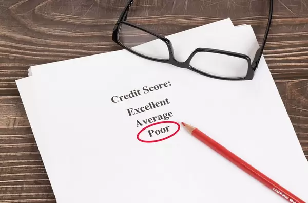 Weißes Papier mit schlechtem Kreditscore-Ergebnis rot umkreist mit Lesebrille und rotem Holzstift auf einem Holztisch
