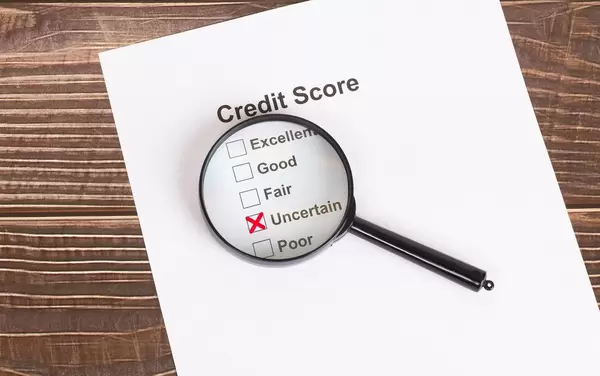 Weißes Papier mit ungewissem Kreditscore-Ergebnis unter einer Lupe auf einem Holztisch