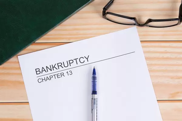 Weißes Papier mit Wort Bankruptcy mit Kugelschreiber und Lesebrille auf einem Holztisch