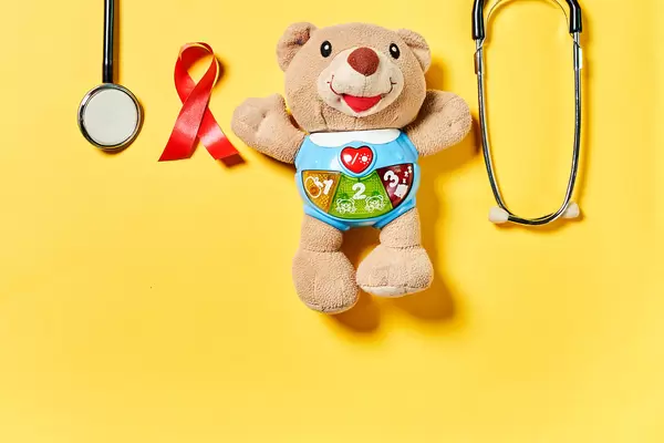 Weltkrebstag - 4. Februar: rote Schleife, medizinische Ausrüstung, Kuscheltier vor gelbem Hintergrund