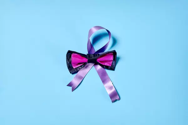 Weltkrebstag am 4. Februar: eine lila Schleife mit rosa-schwarzer Fliege vor blauem Hintergrund