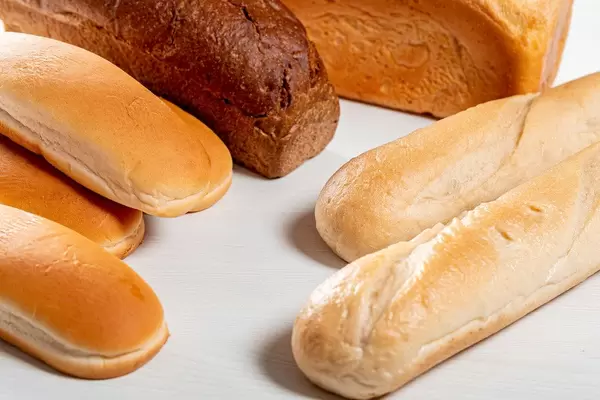 Wheat bread, rye bread, baguettes and buns for hot dogs on white wooden background