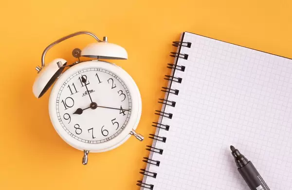 White alarm clock on yellow background with empty notepad