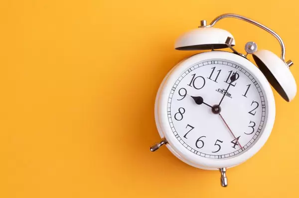 White alarm clock on yellow background with empty space