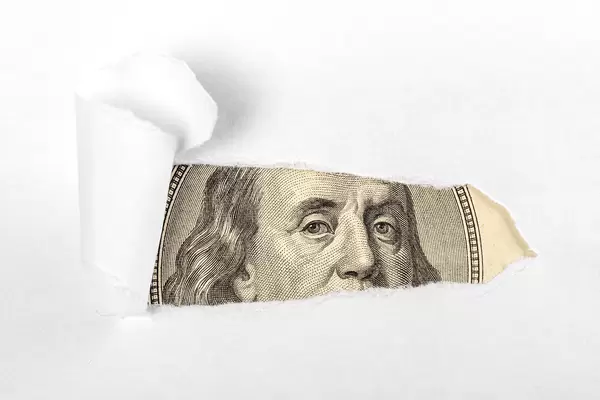 White background, from under which a portrait depicted on a hundred dollar bill peeps