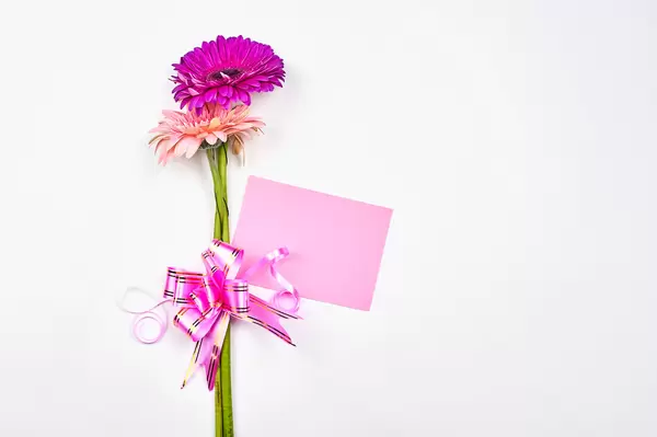 White background with pink flowers, pink ribbon and pink card: space for a romantic message