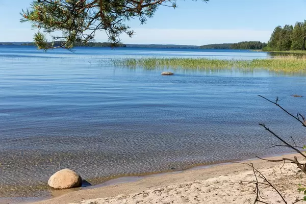 White beach in the bay of Kelvenne Island, with stones in the blue lake, reeds and Päijänne National Park, Finland, in the background