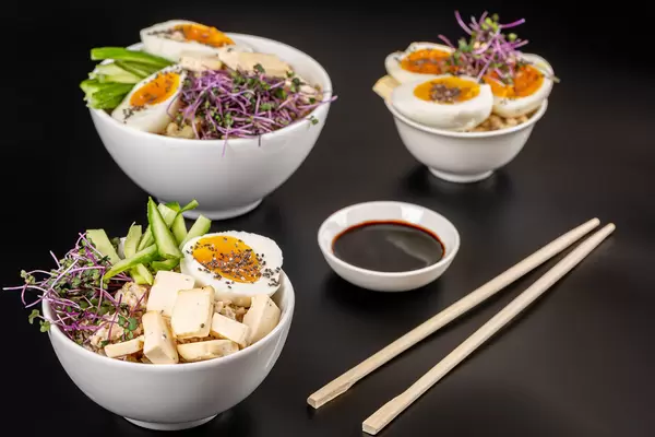 White bowls with oatmeal, cabbage microgreens, cucumber, cheese and boiled eggs on a dark background