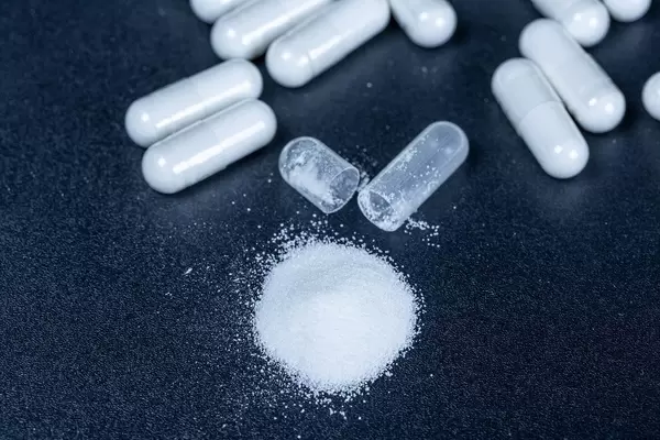 White capsules with powder and one open on a black background
