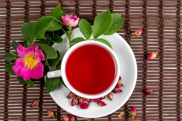 White cup of tea and tea rose on bamboo tablecloth, top view