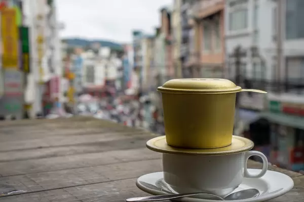 White Cup with Spoon, Saucer and Vietnamese Coffee Filter with City View in the Background